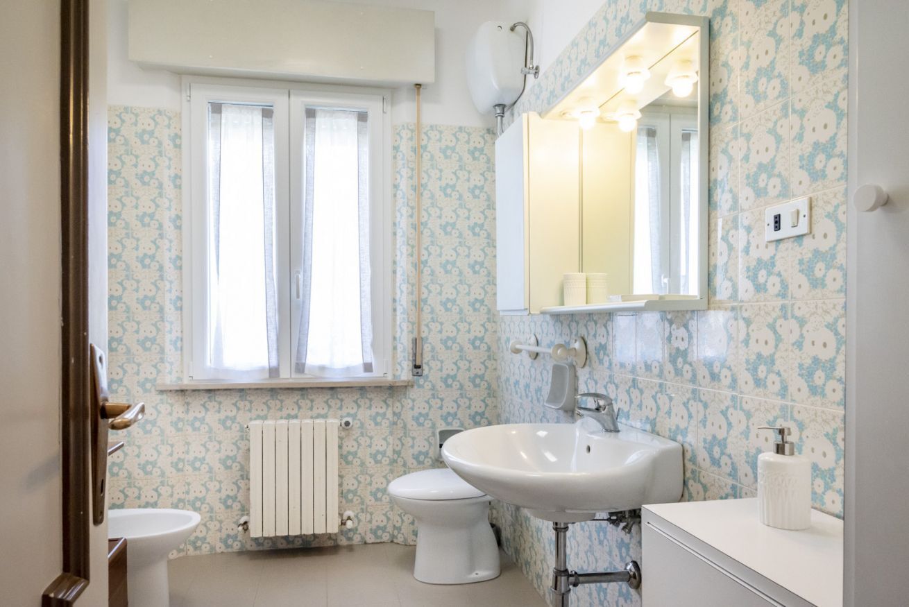 A bathroom with a toilet, sink, and window.