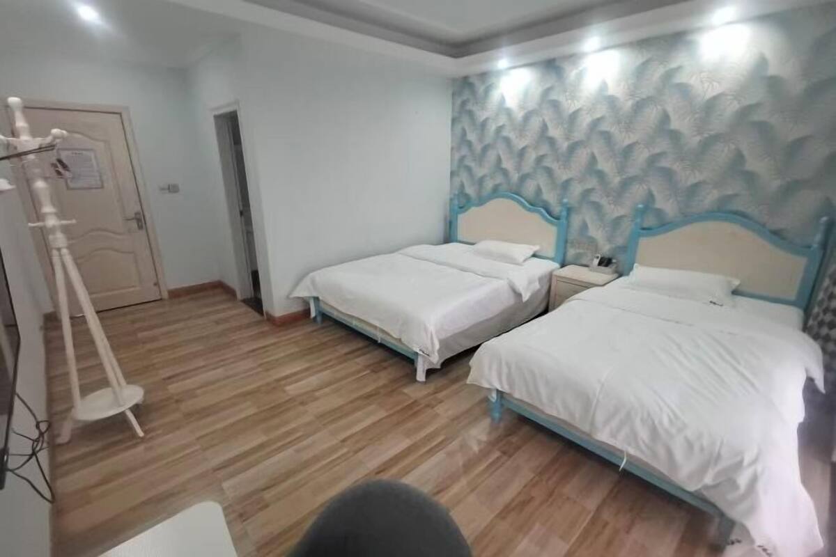 Habitación de hotel con dos camas individuales, piso de madera, un adorno en la pared y una puerta con un cartel.