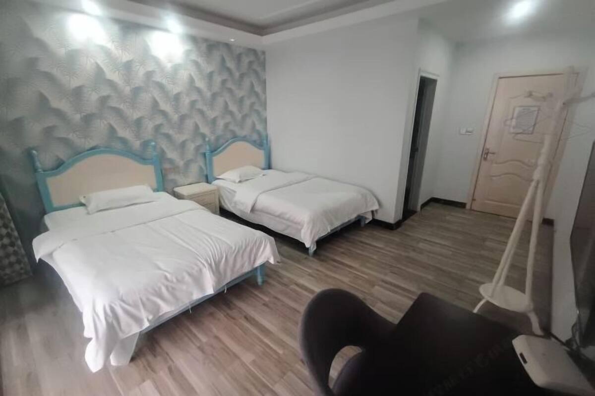 Habitación de hotel con dos camas individuales, suelo de madera, una silla y una cortina.