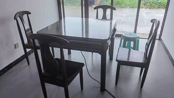 A dining area with a table and four chairs, a green stool, and a view through a glass door.