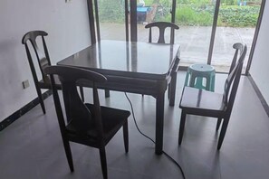 A dining area with a table and four chairs, a green stool, and a view through a glass door. - Xinchang Yunqi Small Building House (Xinchang)