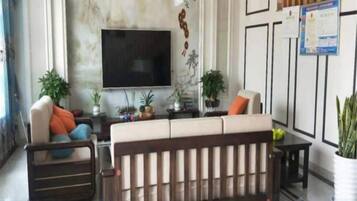 A living room with a sofa, a television, and decorative plants.