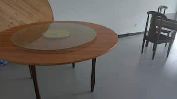 A round wooden table with a glass top, a wooden chair, and a plain white wall in the background.