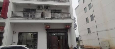 Un edificio de varios pisos con una entrada central, balcones en los niveles superiores y un automóvil estacionado adelante.