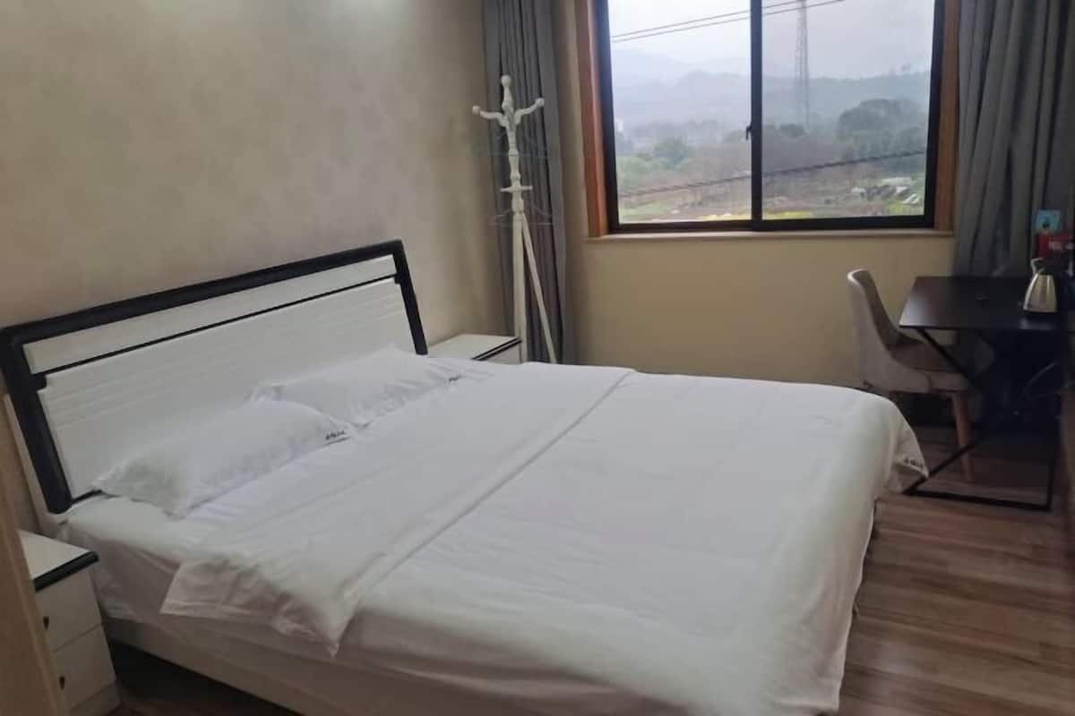 Una cama bien hecha con sábanas blancas en una habitación con suelo de madera, un escritorio y una silla.