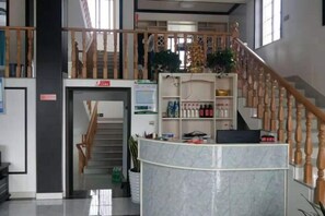 A reception area with a marble counter, a staircase with wooden railings, and a shelf with various items including bottles and a plant. - Xinchang Yunqi Small Building House (Xinchang)