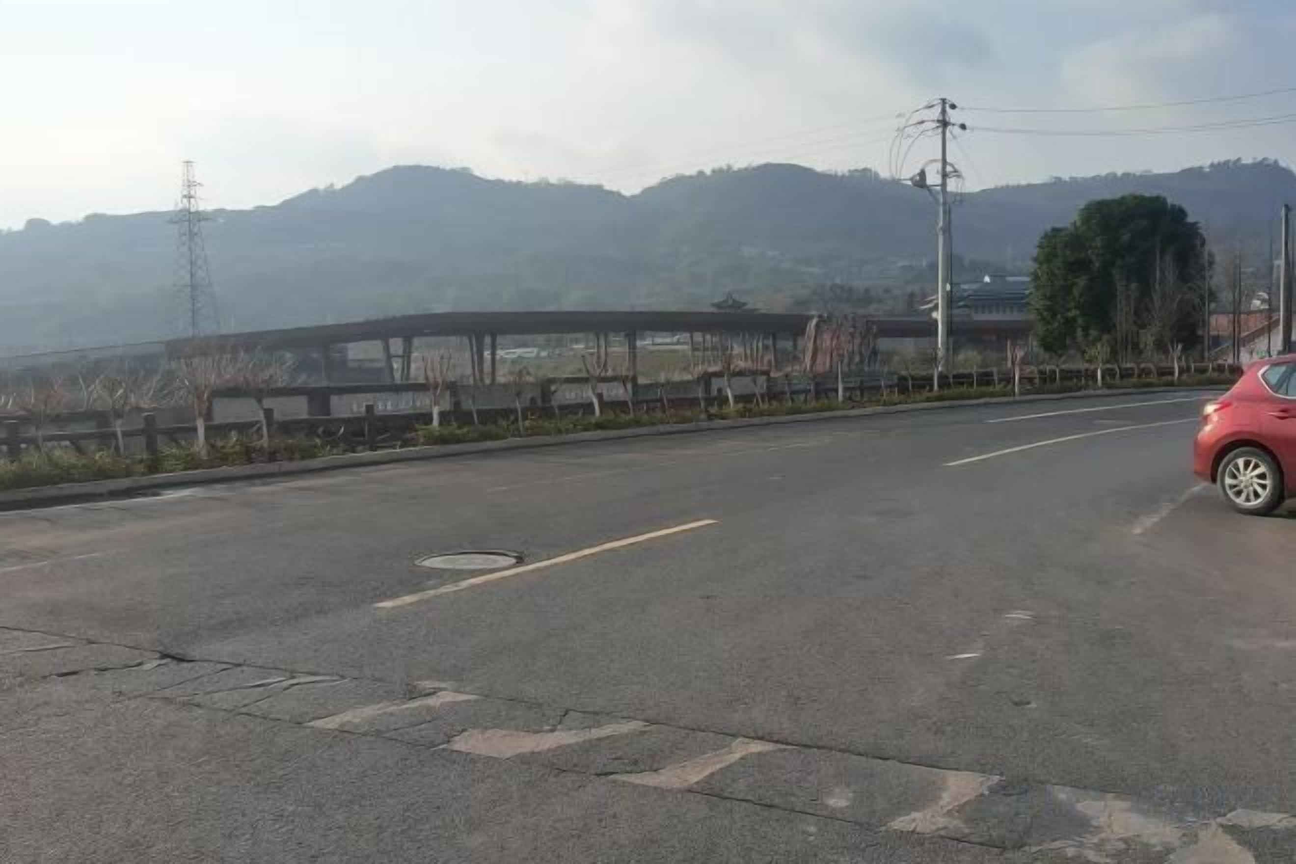 A road with a pedestrian bridge and a red car parked on the side.