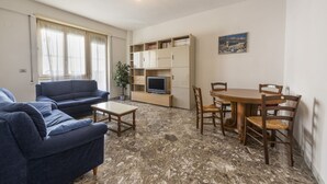 Een woonkamer met een bank, salontafel, tv-meubel en een eettafel met stoelen.