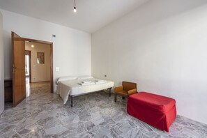 Un dormitorio con cama, una silla y un reposapiés rojo.