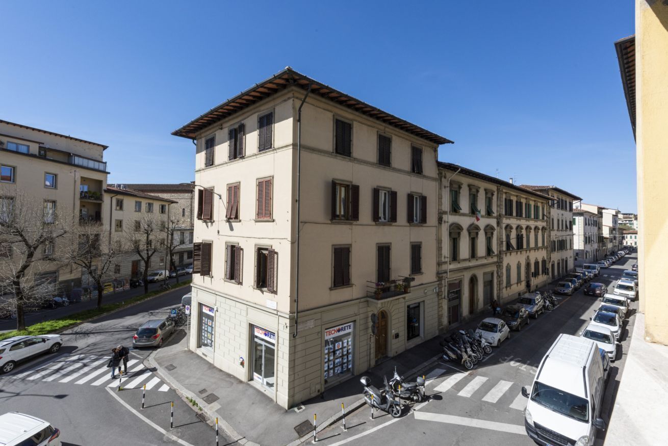A multi-story building with a ground-floor shop, parked cars, and a clear sky.