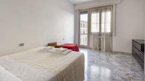Een hotelkamer met een bed, een kleintje tafeltje, een stoel, een kapstok en uitzicht door een raam.