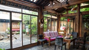 A spacious room with large windows, wooden beams, a sofa, chairs, and a table. - Baisha No. 66 Post Station (Yulong)