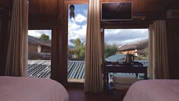 A room with two beds, a TV, and a view of traditional buildings outside.