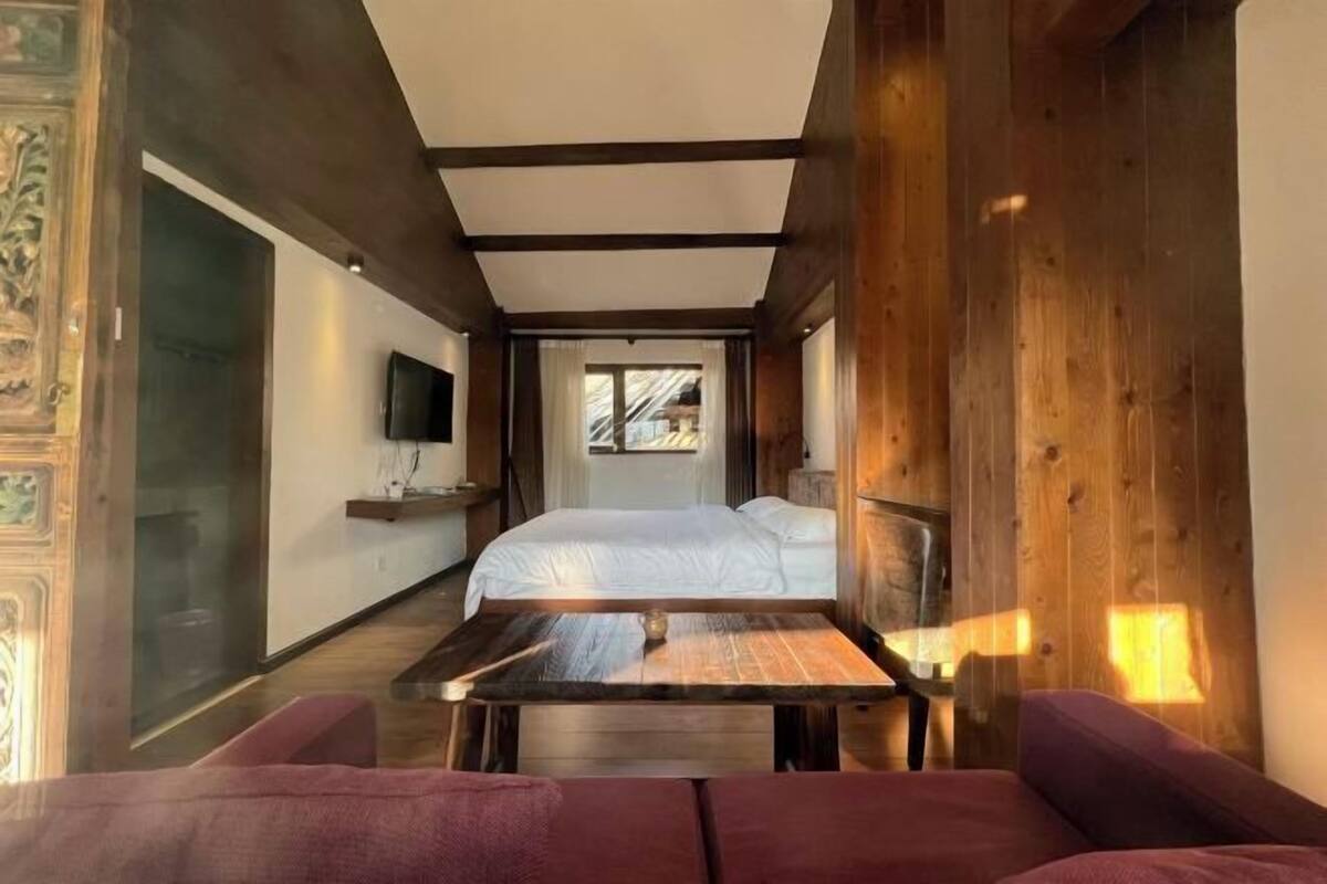 Una habitación de hotel moderna con una cama grande, una mesa de madera y vistas al exterior.