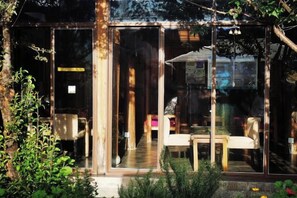 A glass-walled room with a bench and a table, a wooden door, and a view of the outdoors.