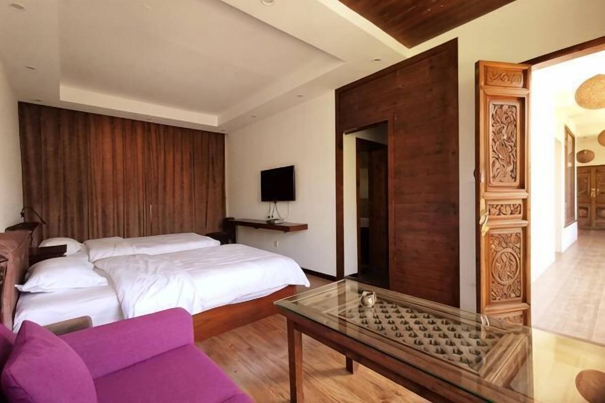 Un dormitorio con una cama, un televisor, una puerta de madera y una mesa de centro de vidrio.