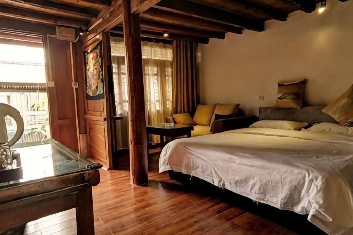 Habitación con cama, una mesita y una silla. Se ve una ventana con cortinas y vistas al exterior.