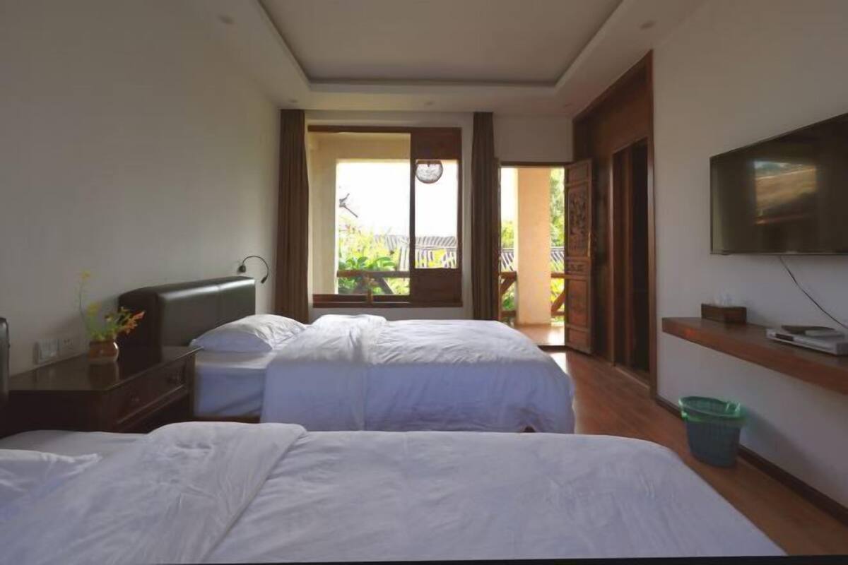 Habitación de hotel con dos camas, televisión, escritorio y balcón con vistas.