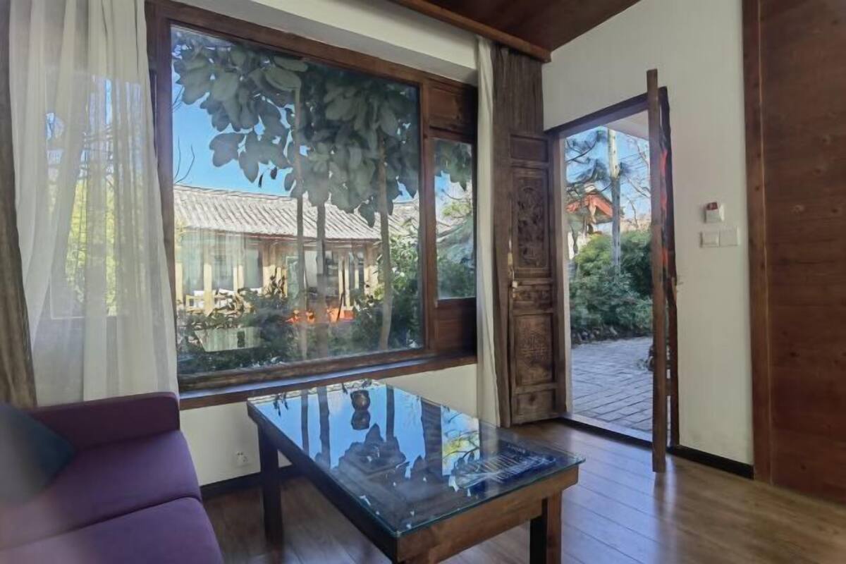 Una habitación con una mesa de vidrio, un sofá púrpura y vistas a un edificio tradicional a través de un ventanal grande.