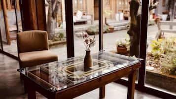 A room with a glass-top table, a vase with flowers, a chair, and a view of the outdoors.