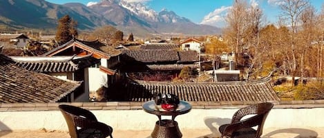 A terrace with a table and chairs overlooking a traditional village with buildings and mountains in the background.