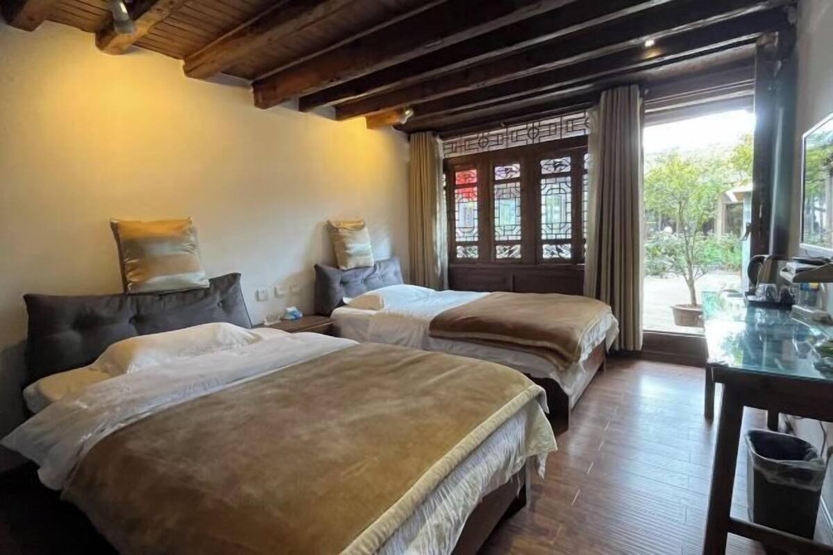 Una habitación con dos camas, piso de madera, un ventanal con detalles decorativos y una mesa con un cubo de basura.