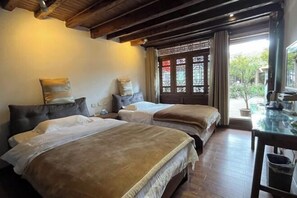 Una habitación con dos camas, piso de madera, un ventanal con detalles decorativos y una mesa con un cubo de basura.