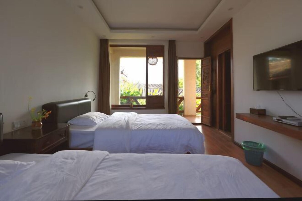 Habitación de hotel con dos camas, televisión, escritorio y balcón con vistas.