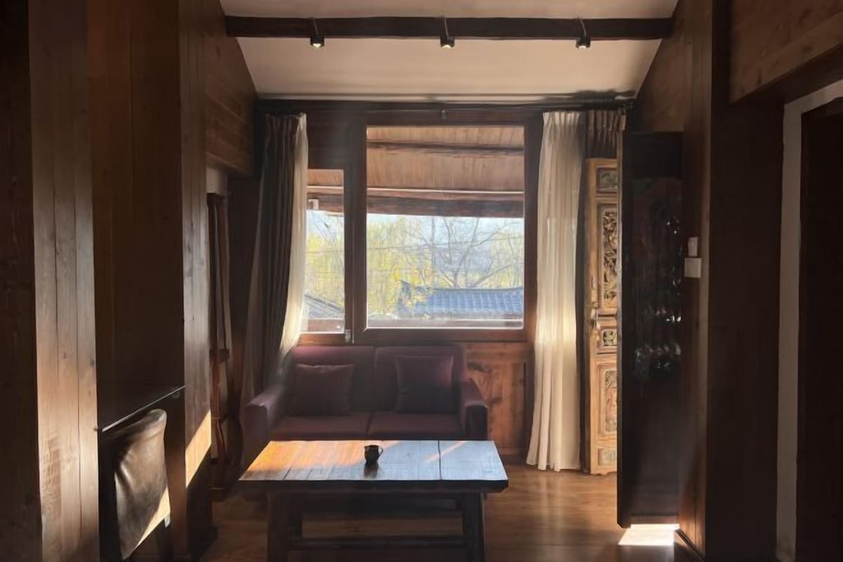 Una habitación acogedora con detalles de madera, un sofá, una mesa y una ventana con cortinas.