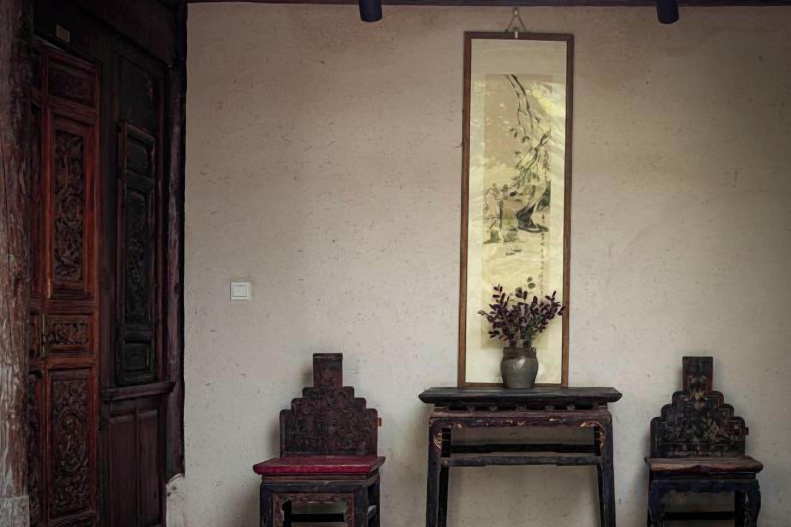 A traditional room with a wooden door, a framed painting, and two small tables with decorative items.