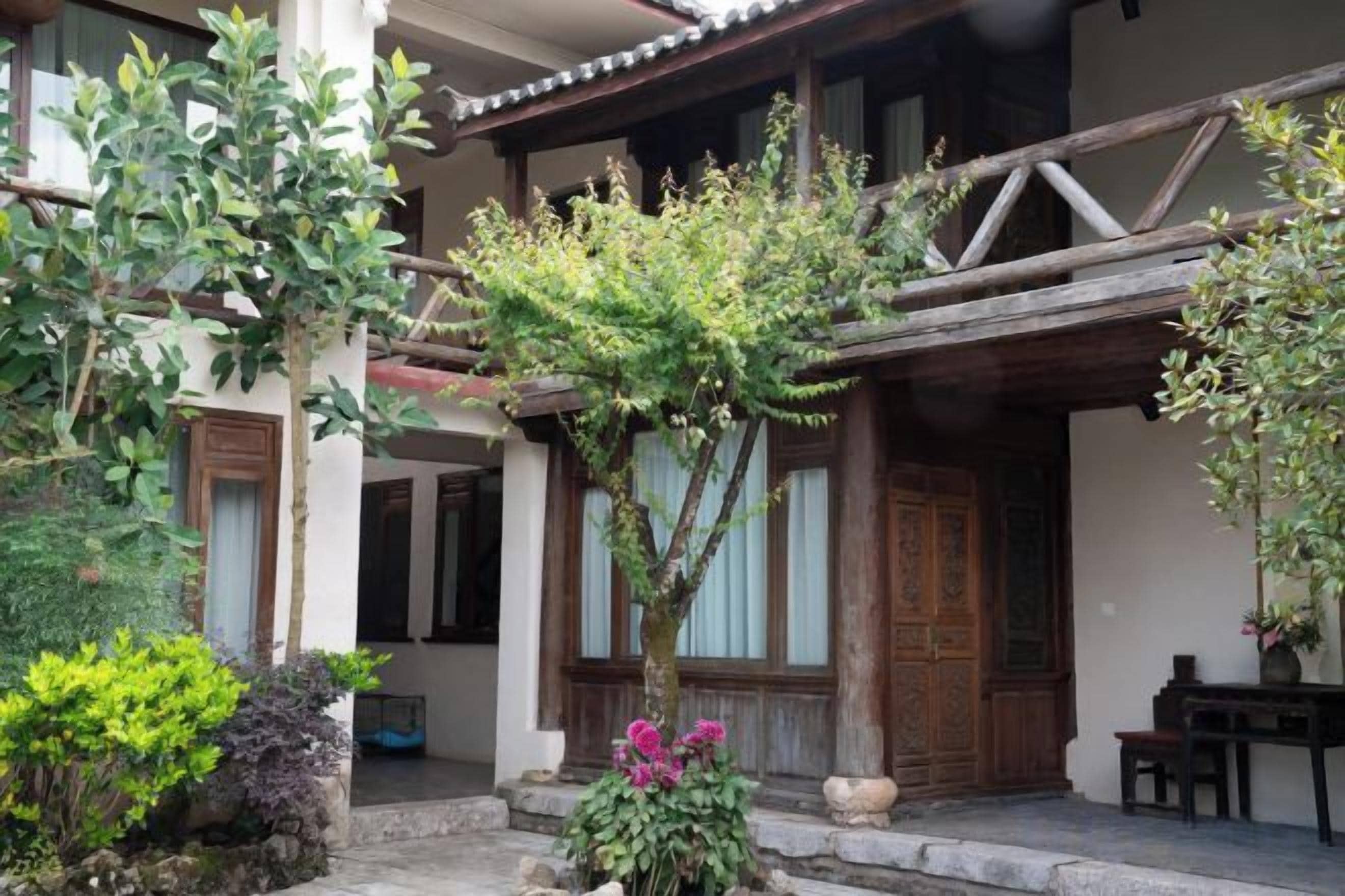 Un edificio tradicional con fachada de madera, un porche cubierto y un pequeño jardín con diversas plantas.