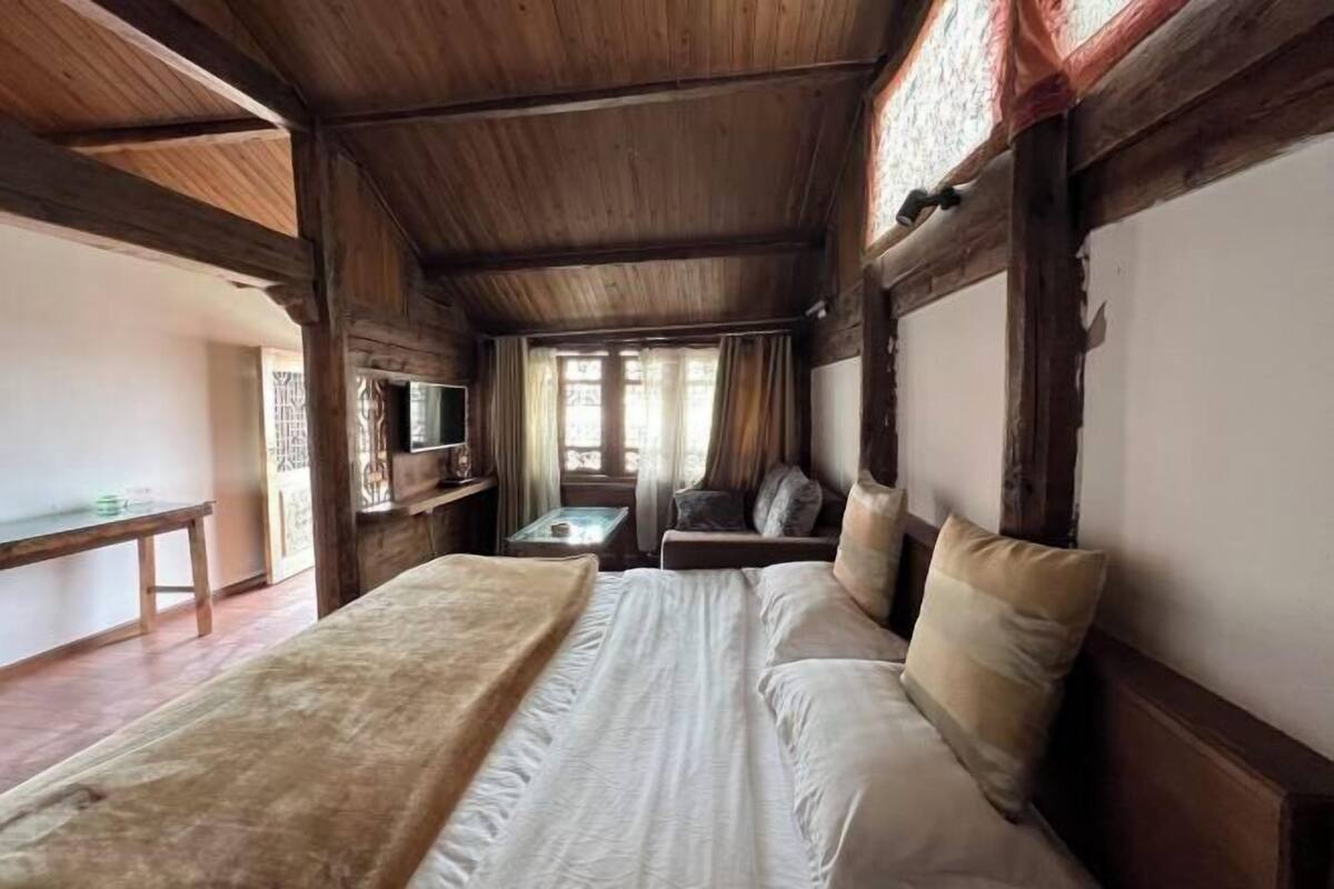 Una habitación con una cama, una mesita, un banco y una ventana con cortinas.