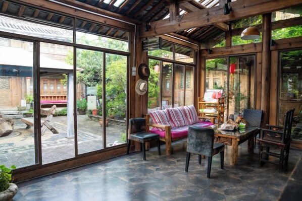 A room with a large glass door leading outside, a wooden ceiling, and a seating area with a sofa and chairs.