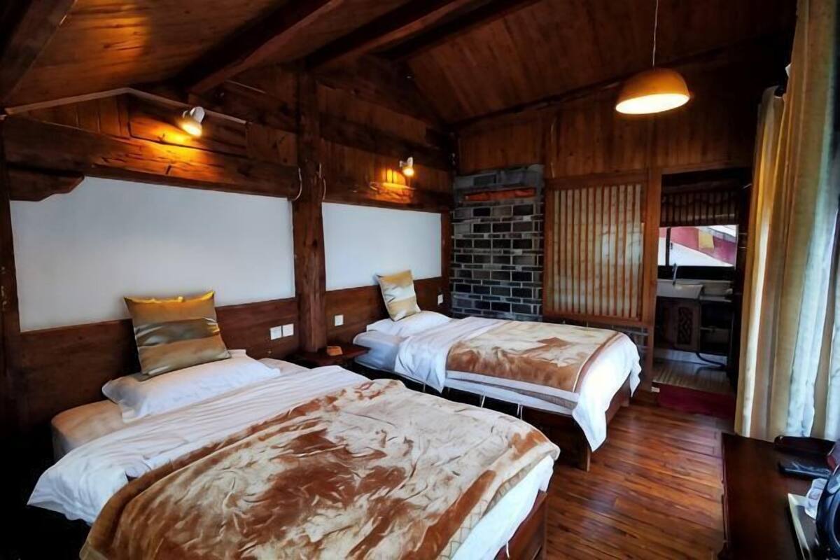 Una habitación con dos camas, paredes de madera y una pared de ladrillo, con una lámpara colgante.