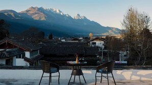 A traditional building with a sloped roof, a table with chairs, and a view of mountains in the background. - Baisha No. 66 Post Station (Yulong)
