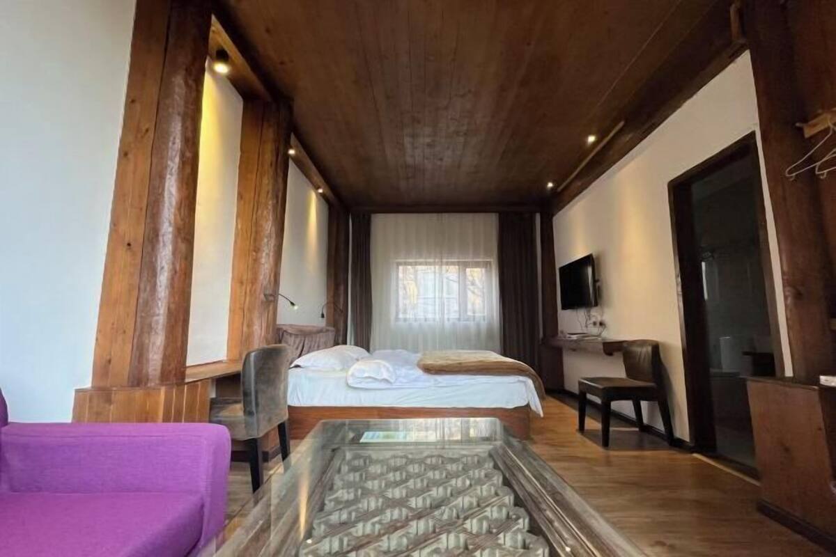 Una habitación con cama, una silla, televisor y techo de madera.