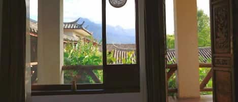 A room with a bed, a window with a view of traditional architecture and mountains.
