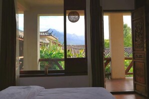 Una habitación con cama, ventana y vistas a arquitectura tradicional y montañas.