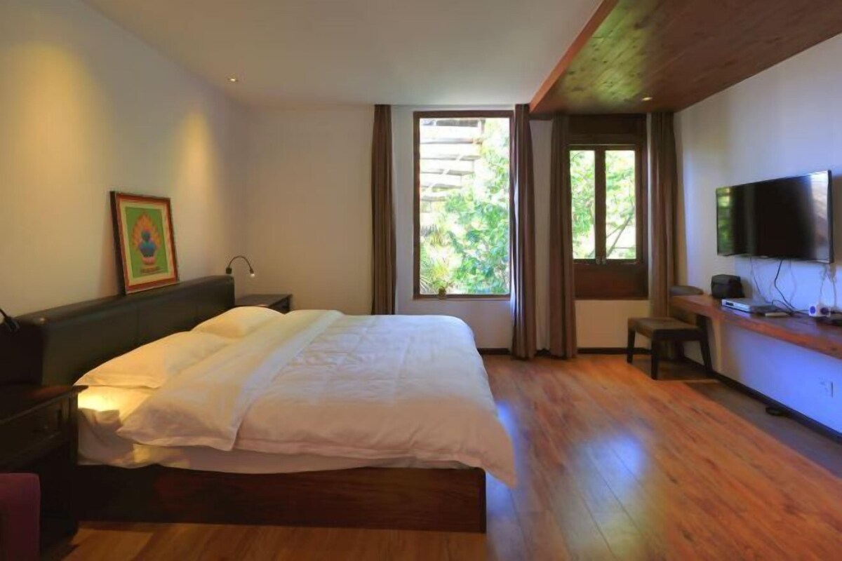 Un dormitorio con cama, escritorio, televisor y ventana con vistas a la vegetación.