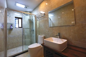Un baño con ducha de vidrio, lavamanos blanco y un espejo grande.
