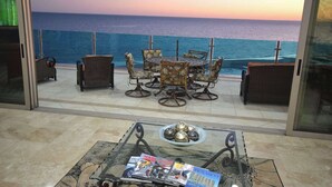 A terrace with a view of the sea, featuring a table with magazines, a bowl of decorative balls, and wicker chairs.