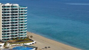 A high-rise hotel with multiple balconies overlooking a beach and a pool area.