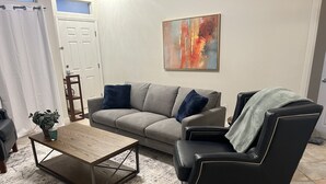 Ein Wohnzimmer mit grauem Sofa, einem schwarzen Ledersessel, einem Holztisch und einem Bild an der Wand.