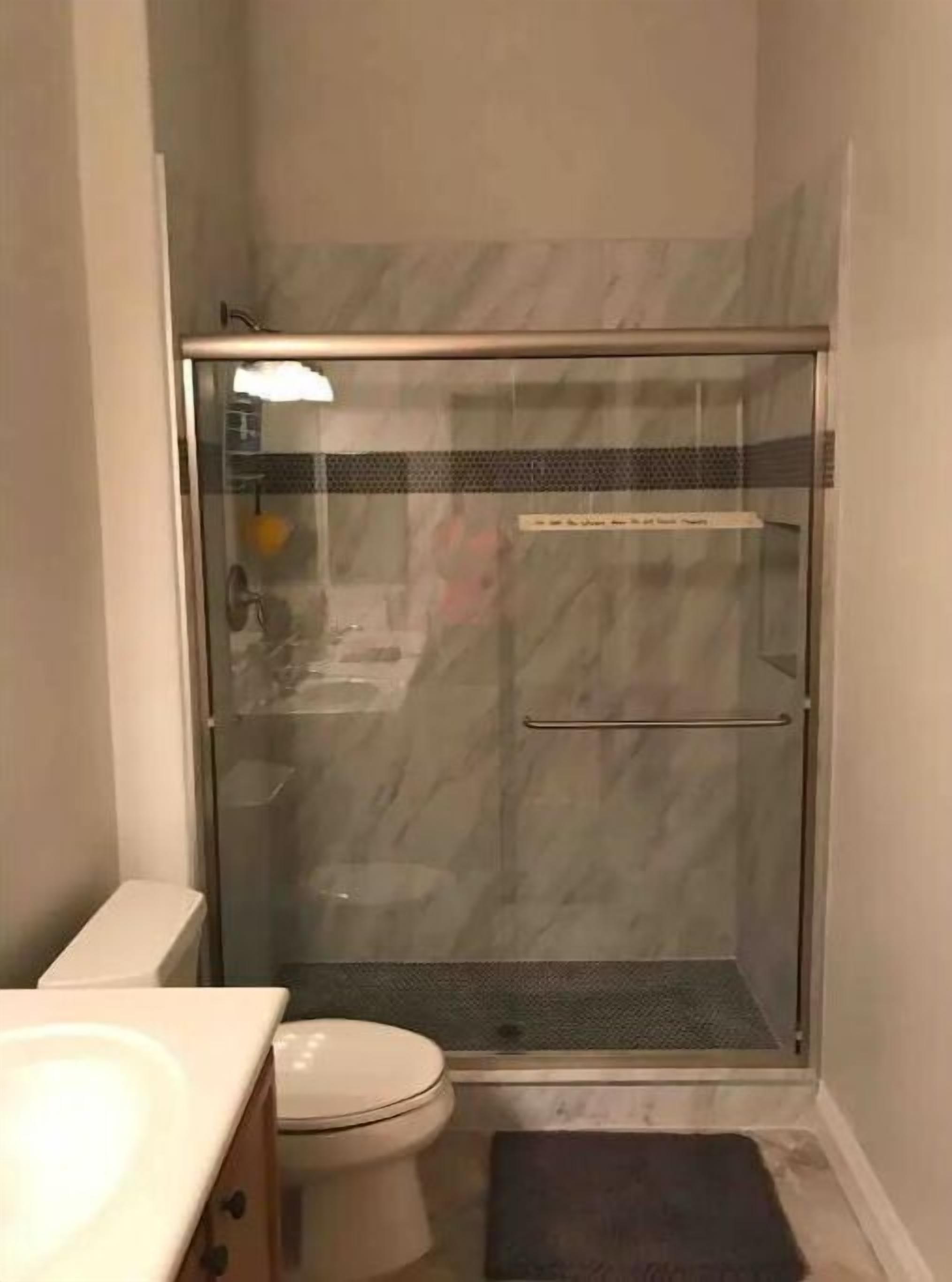 A bathroom with a glass-enclosed shower, a toilet, and a sink.