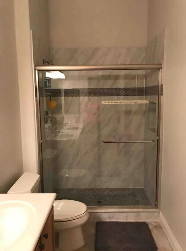 A bathroom with a glass-enclosed shower, a toilet, and a sink.