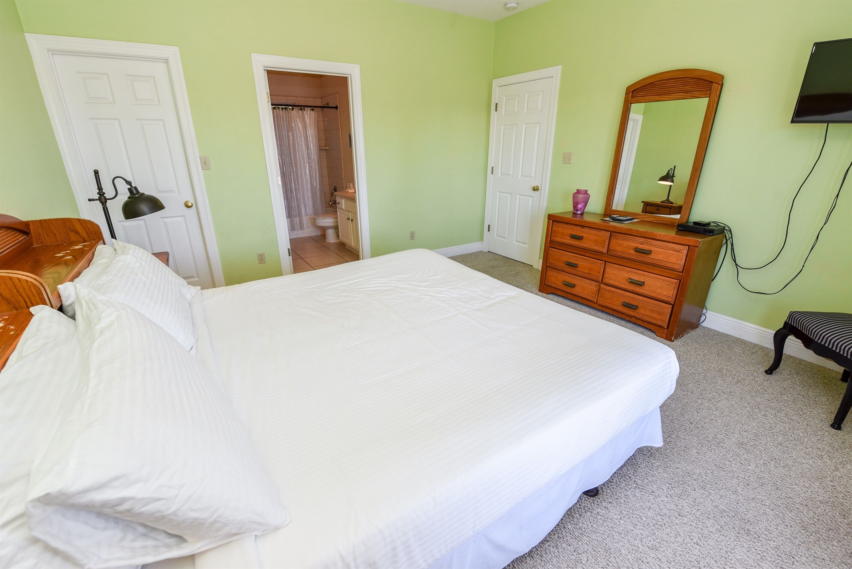 Une chambre à coucher avec un grand lit, une commode en bois, un miroir et un téléviseur fixé au mur.