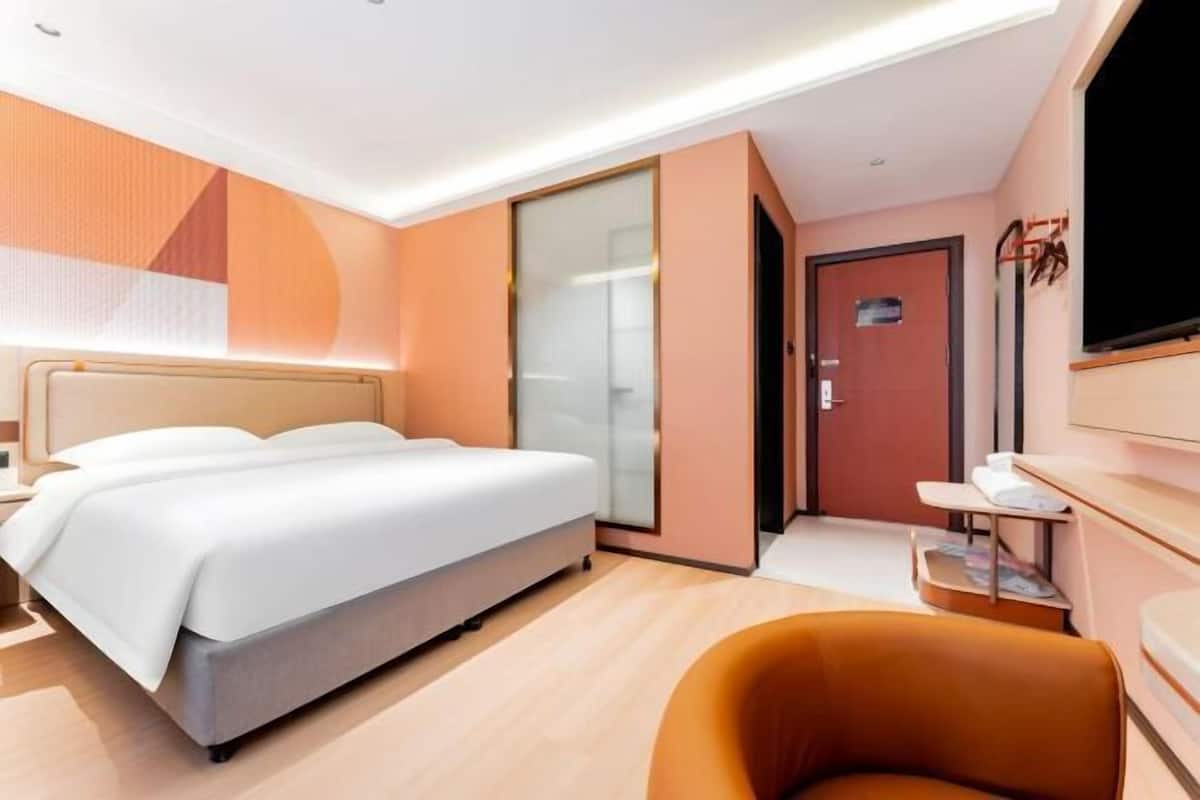Ein modernes Hotelzimmer mit Bett, Fernseher, Schreibtisch und Tür.