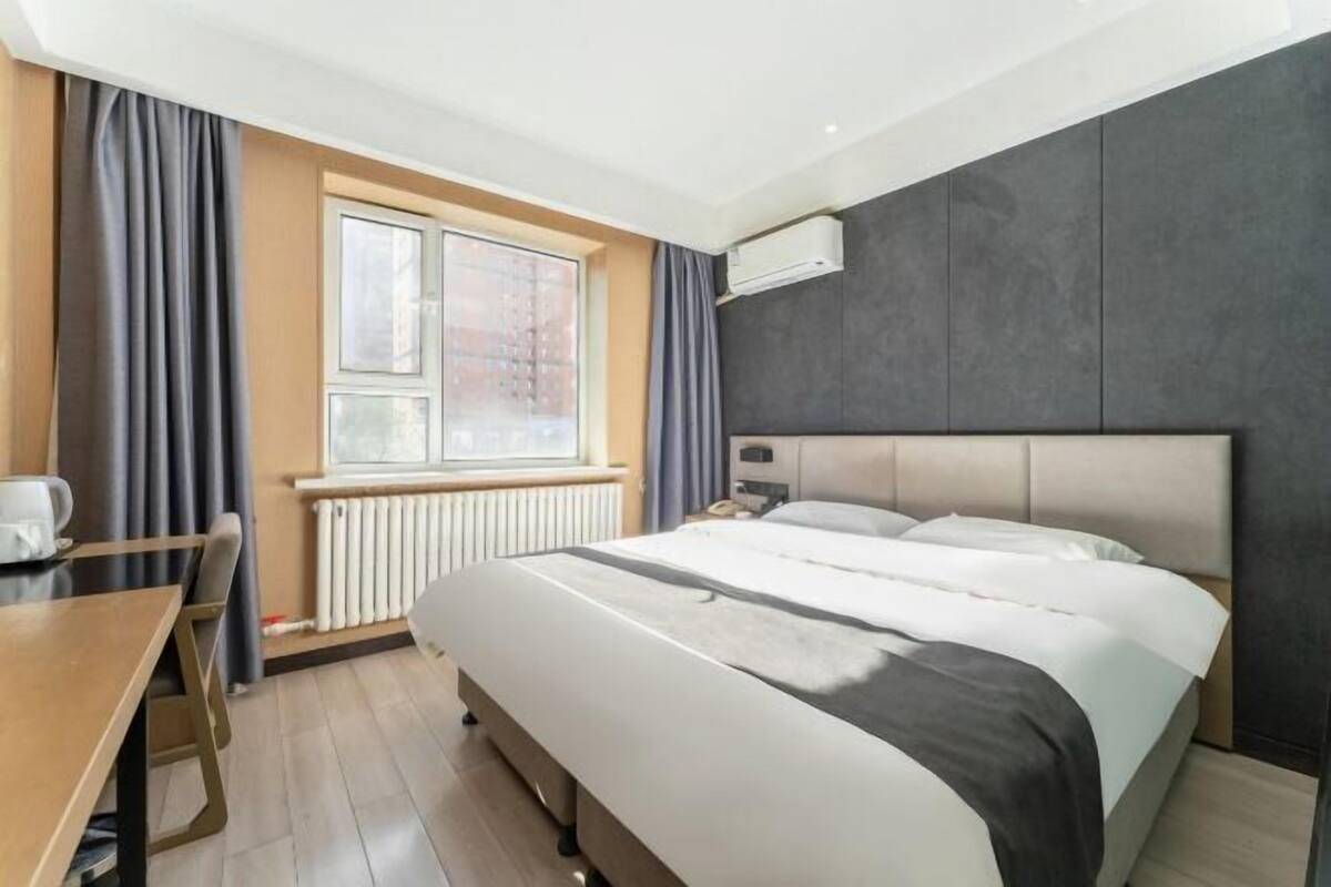 Ein Hotelzimmer mit Bett, Schreibtisch, Fenster mit Vorhängen und Klimaanlage.
