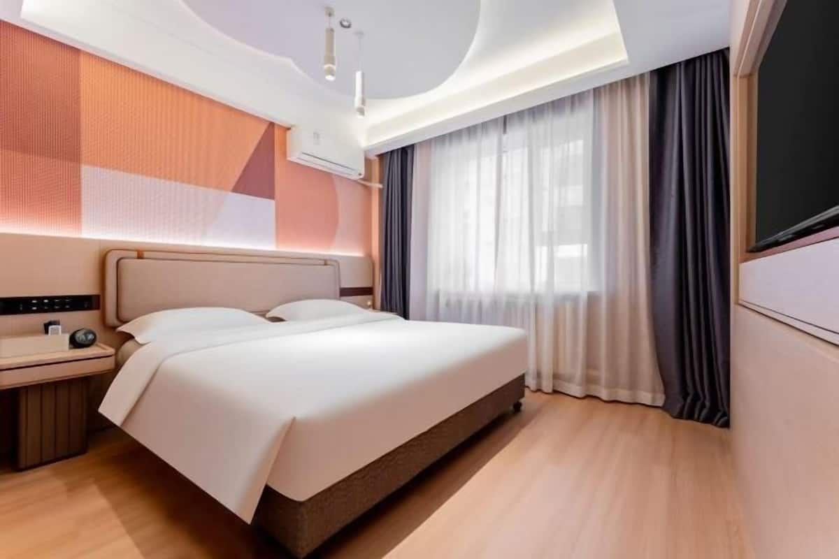 Ein modernes Hotelzimmer mit Bett, Nachttisch und einem großen Fenster mit Vorhängen.
