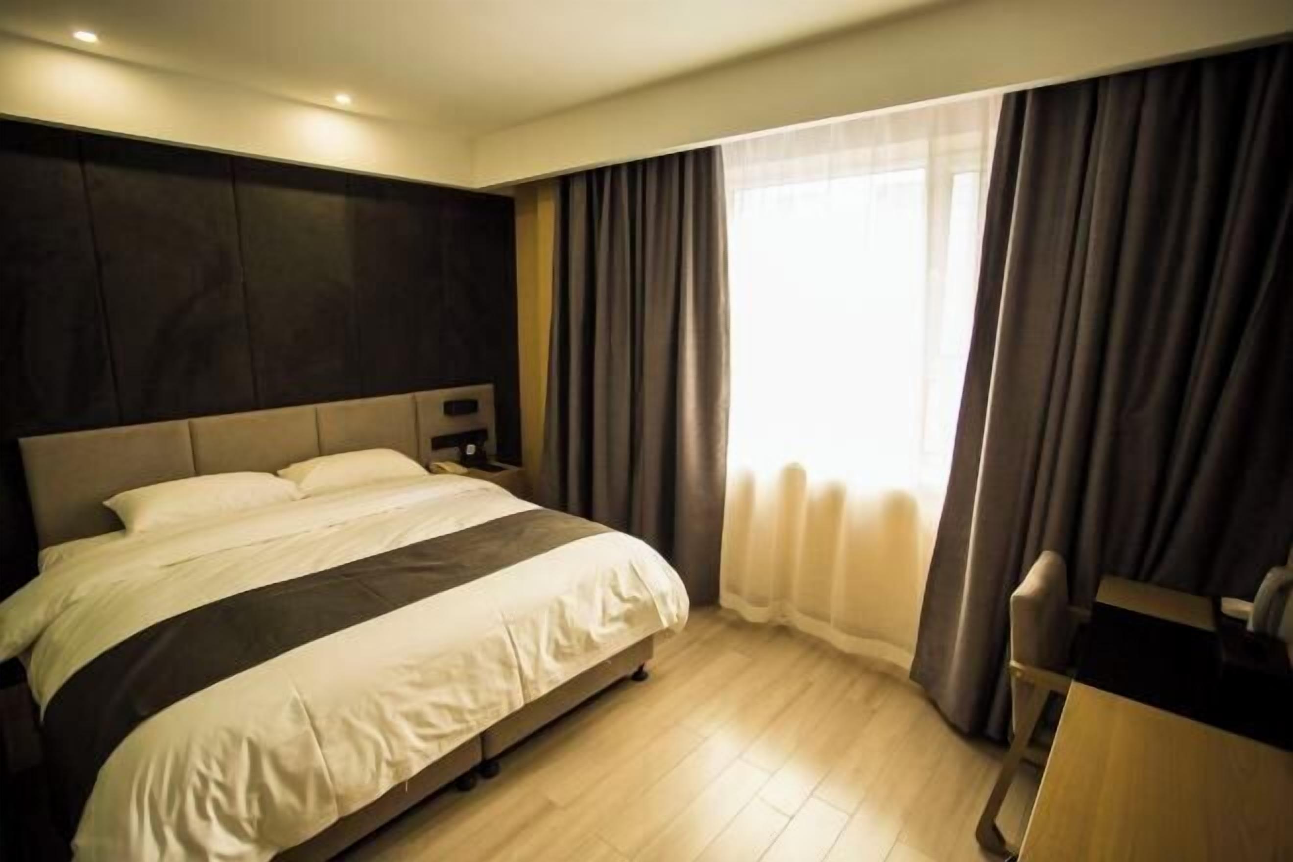 A hotel room with a large bed, a desk, and a window with curtains.